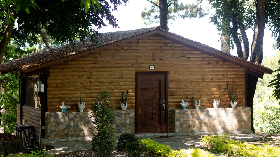 Cabaña de madera en Villa Shalom, rodeada de plantas y árboles, con una puerta de entrada y un ambiente natural.