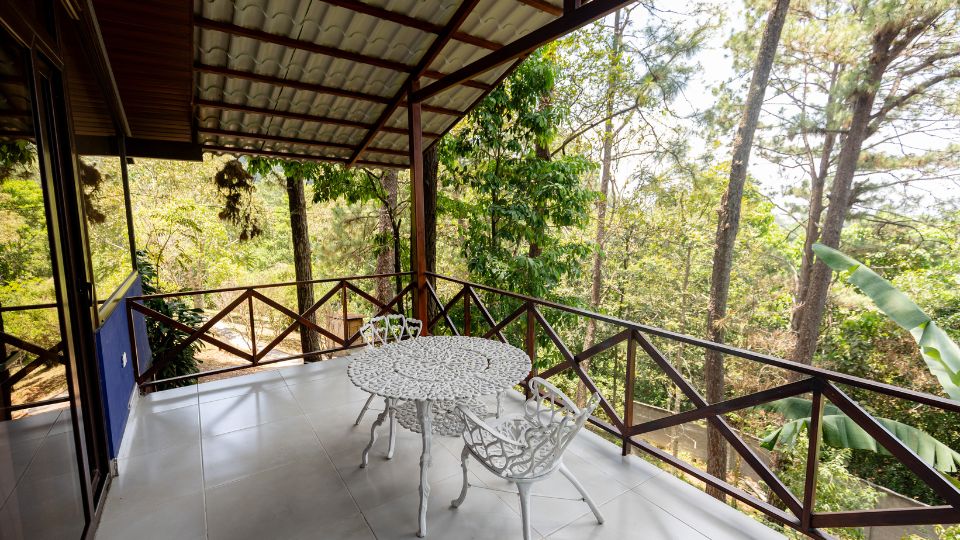 Terraza de Villa Shalom en Santa Rosa de Copán, Honduras, con mesa y sillas de diseño, rodeada de árboles y naturaleza.
