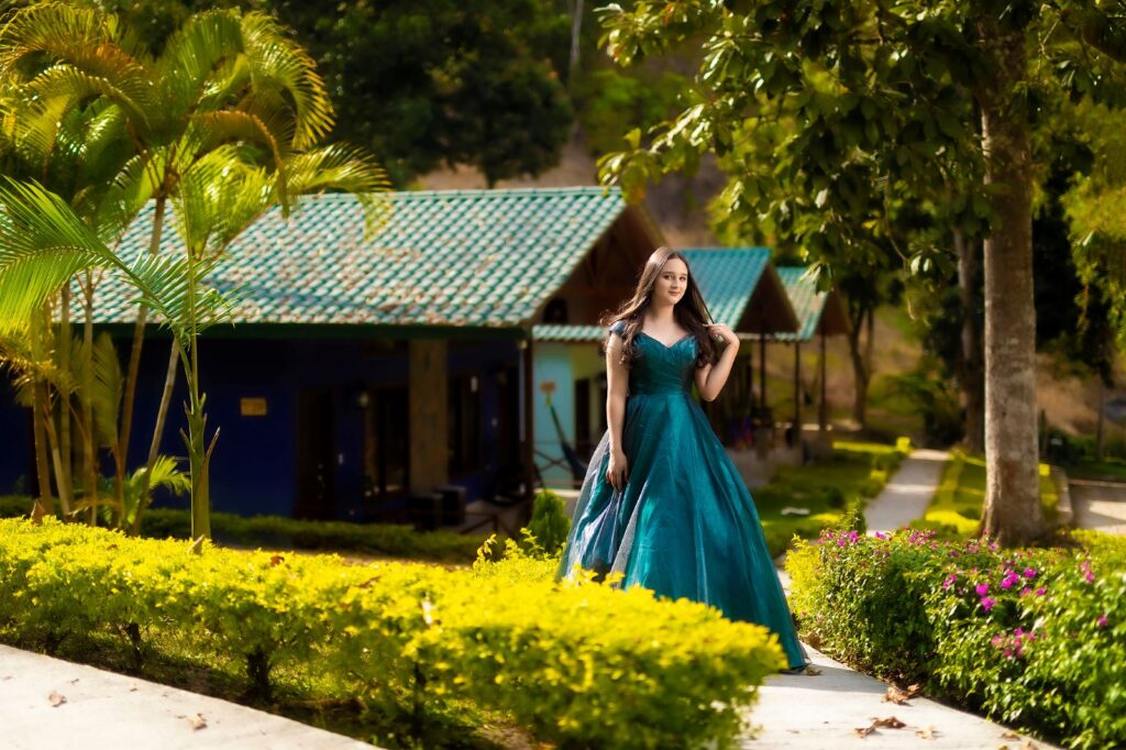 Joven vestida con un elegante vestido azul posando en el jardín de Villa Shalom, rodeada de cabañas y vegetación en Santa Rosa de Copán.