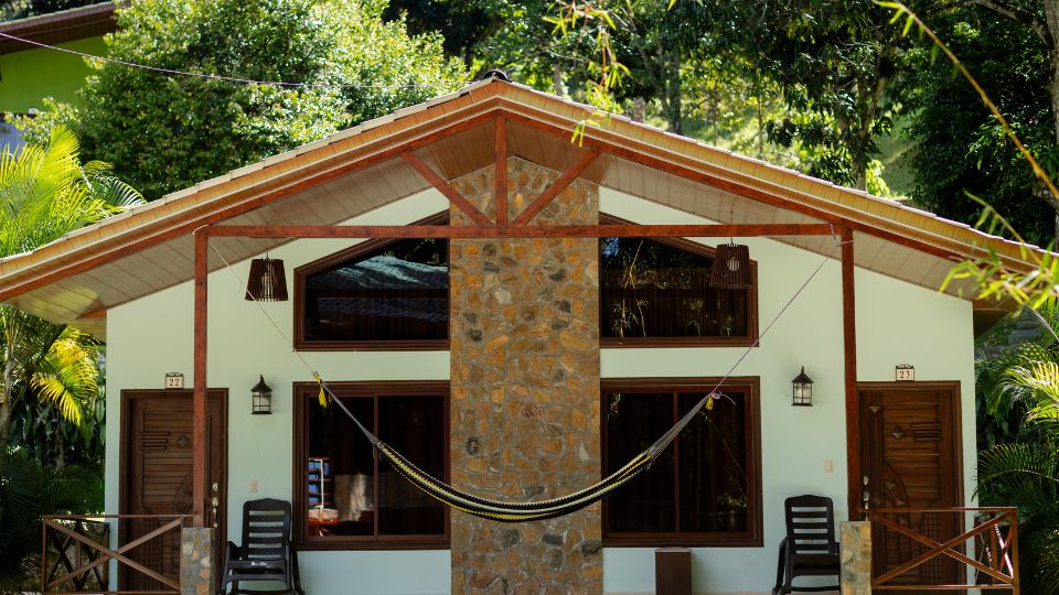 Cabaña de Villa Shalom en Santa Rosa de Copán, Honduras, con un diseño de madera y piedra, y una hamaca colgante entre dos postes.