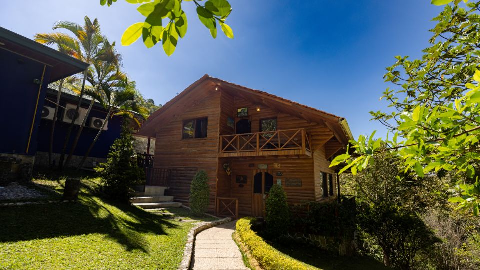 Cabaña de madera en un entorno natural, rodeada de jardines y bajo un cielo azul, ubicada en Villa Shalom, Santa Rosa de Copán, Honduras.