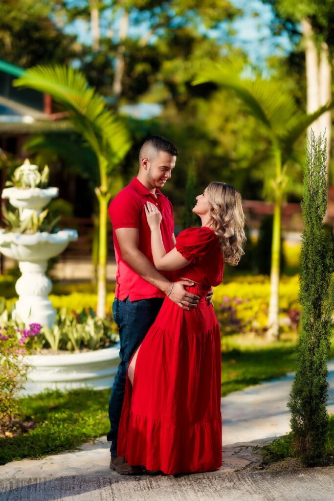 Pareja romántica en un jardín de Villa Shalom, con una fuente al fondo; ella viste un vestido rojo y él una camiseta roja.