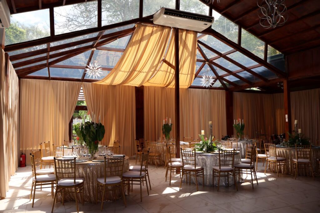 Salón de eventos en Villa Shalom, con mesas decoradas y cortinas que permiten la entrada de luz natural.