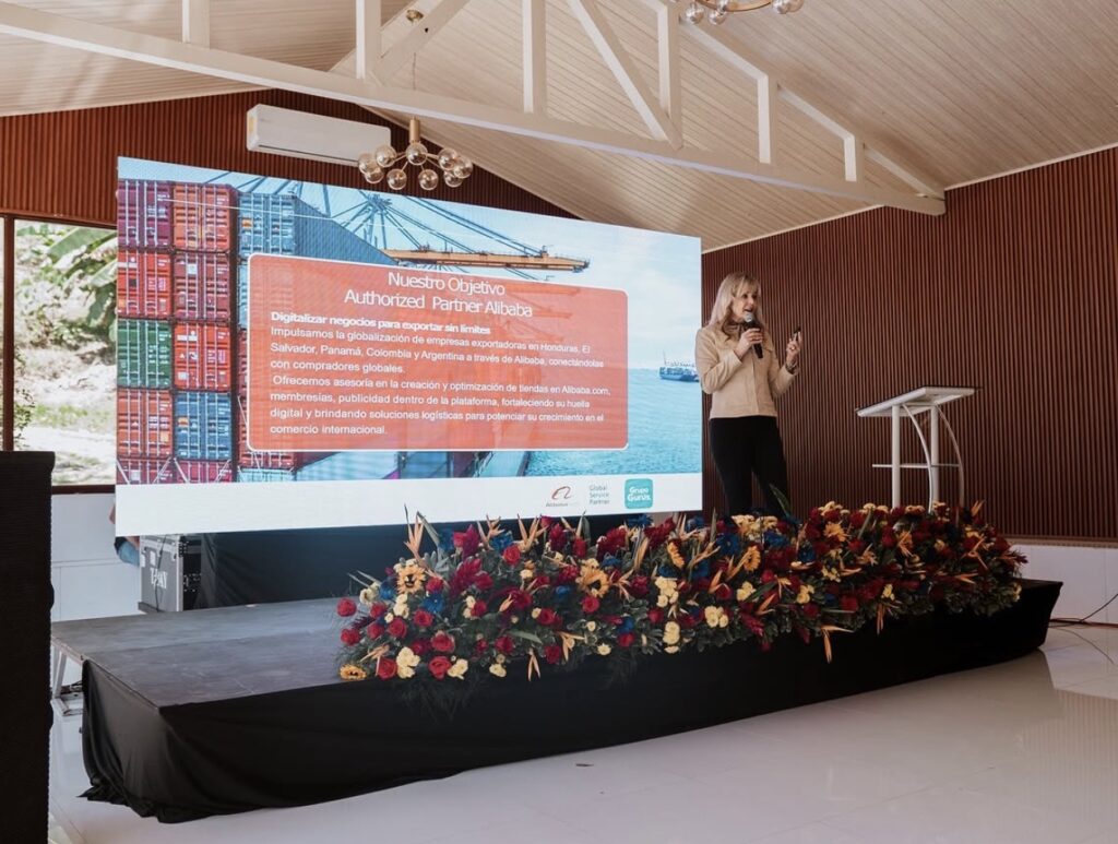 Presentación en Villa Shalom con una mujer de pie frente a una pantalla grande, decorada con flores y un fondo elegante.
