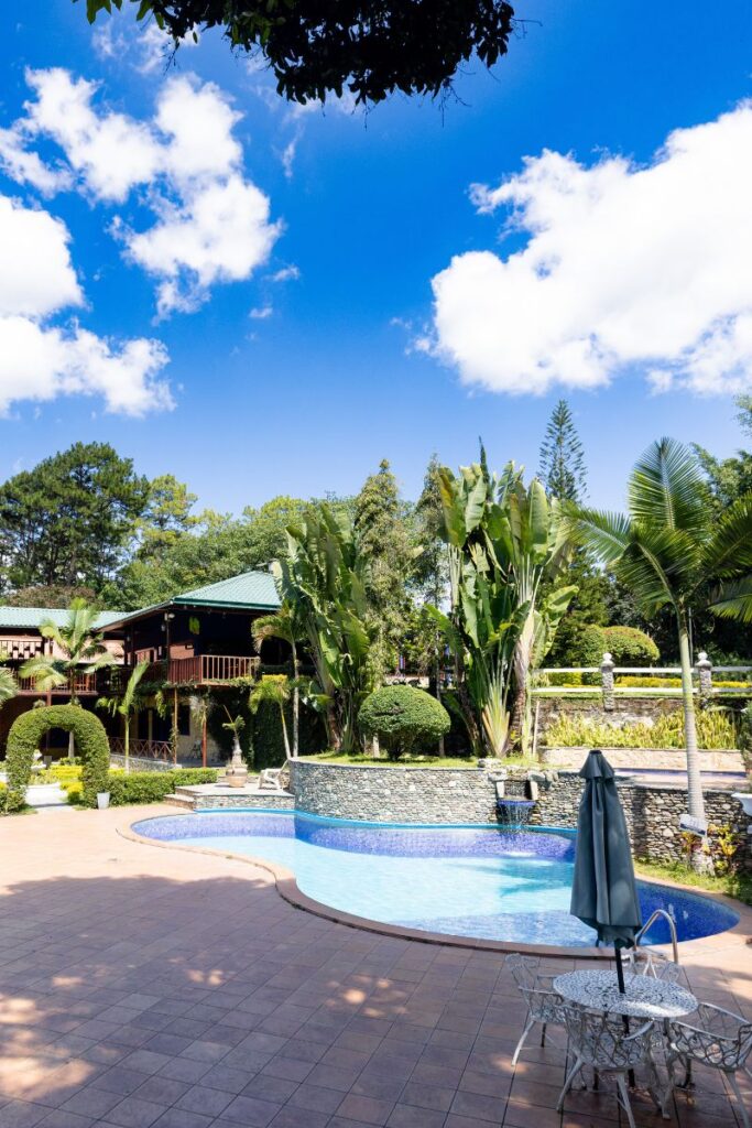 Vista de los jardines de Villa Shalom en Santa Rosa de Copán, Honduras, con palmeras, piscina y un cielo azul despejado.